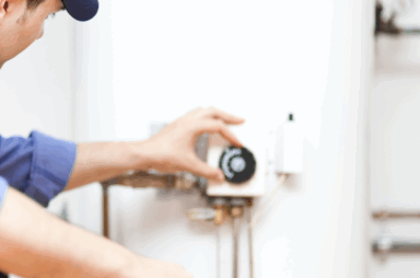 Person adjusting the thermostat on a water heater tank while holding a wrench, wearing a blue uniform and cap—demonstrating common water heater signs that may indicate when to replace your water heater.